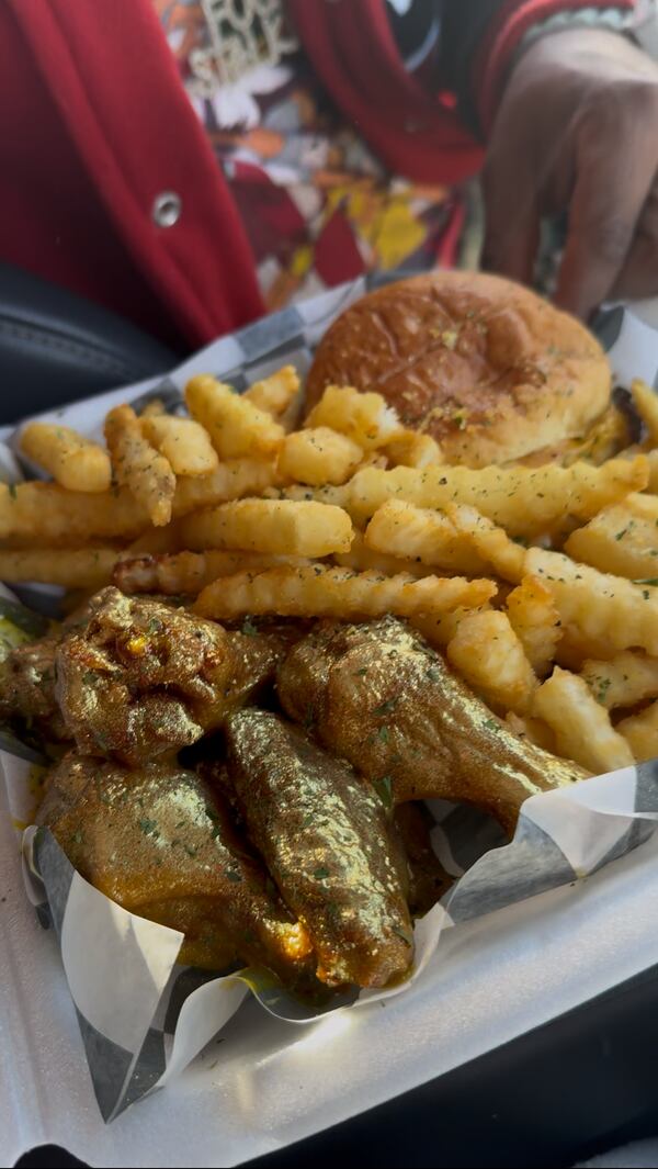 A takeout box of hotwings coated in a golden sauce with crinkle fries