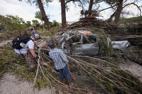 People search around a damaged truck and branches along the Guadalupe River after flooding in Kerrville, Texas on Wednesday , July 9, 2025. (AP Photo/Gerald Herbert)