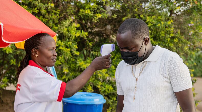 A health worker uses a thermometer to screen a man by the roadside in Bunia, Congo, Tuesday, May 19, 2026. (AP Photo/Moses Sawasawa)