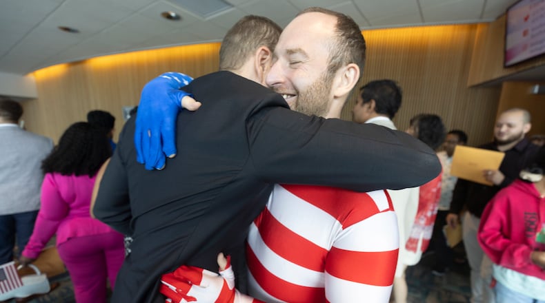 Jima Parkis, dressed in an American flag, hugs his friend James Watson, who emigrated from England, after the Naturalization Ceremony for 150 new citizens in the Gwinnett Justice and Administration Center auditorium Tuesday July 2 2024. (Steve Schaefer / AJC)