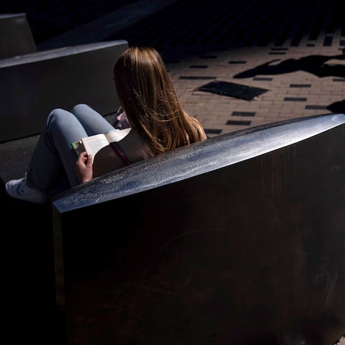 FILE - A woman reads a book in the afternoon sun on a bench outside South Station in Boston, on Friday, May 31, 2024. (AP Photo/David Goldman, File)