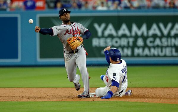 Atlanta Braves' Ozzie Albies, left, turns a double play at second base after forcing out Los Angeles Dodgers' Max Muncy, right, during the second inning of a baseball game Monday, March 31, 2025, in, Los Angeles. (AP Photo/Kevork Djansezian)