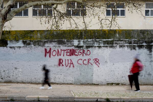 People walk past a graffiti saying "Montenegro Out", referring to Portuguese Prime Minister Luis Montenegro, the day before his government faces a confidence vote in parliament, in Lisbon, Monday, March 10, 2025. (AP Photo/Armando Franca)