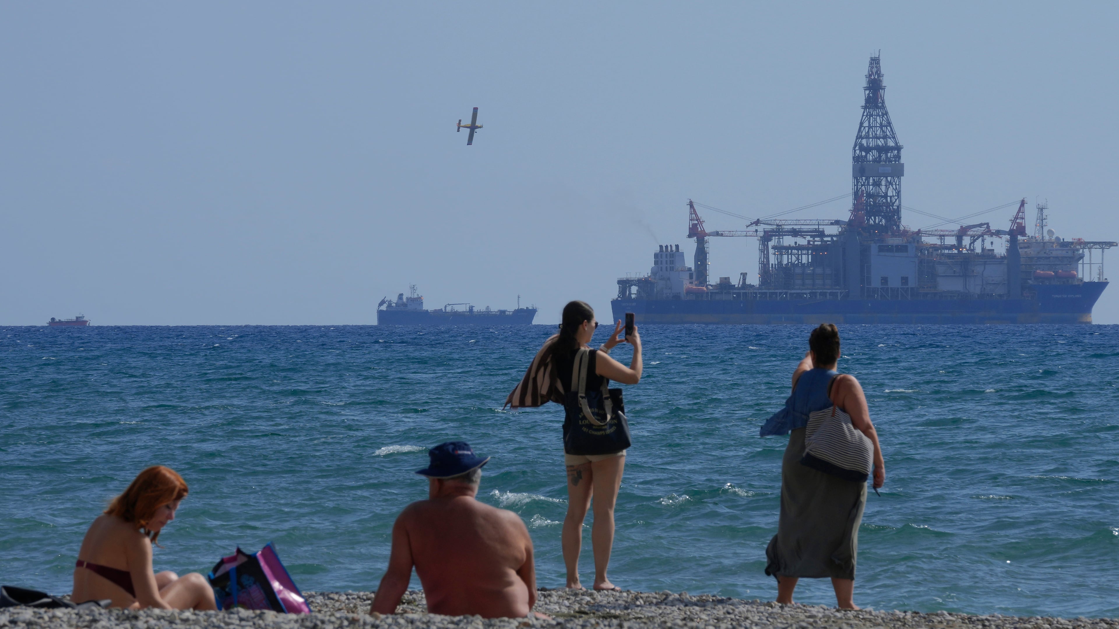 FILE - People on the beach take photos of the 'Tungsten Explorer' drilling ship, in the southern coastal city of Larnaca, Cyprus, Wednesday, Nov. 3, 2021. (AP Photo/Petros Karadjias, File)