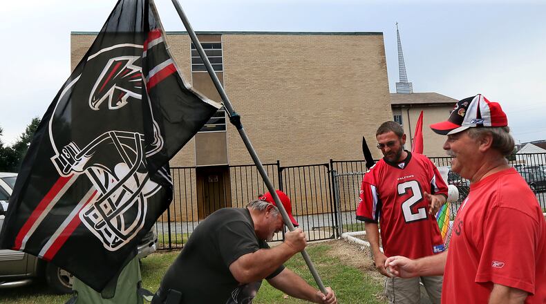 Falcons tailgators Dave Clark (from left), Jonesboro, Pat Blakenship, Villa Rica, and Larry Rinicella, McDonough, raise their Falcons flag beside the Mt. Vernon Baptist Church on Sunday, Sept. 15, 2013, in Atlanta. The group has been renting tailgating space on the church grounds for years. On Thursday, the congregation will vote on whether to accept an offer for the church and move to make room for the new Falcons stadium.