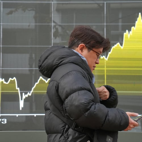A person walks in front of a chart showing Japan's Nikkei index at a securities firm Friday, Dec. 19, 2025, in Tokyo. (AP Photo/Eugene Hoshiko)