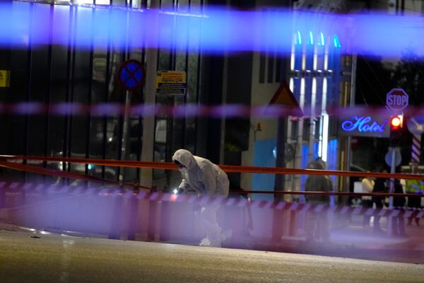 Police investigators wearing coveralls inspect the site after a bomb explosion outside of the Hellenic Train offices the company that runs Greece's railway, the first building on the left, in Athens, Greece, Friday, April 11, 2025. (AP Photo/Petros Giannakouris)
