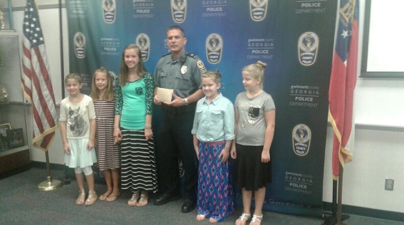 Five of the seven girls who used a lemonade stand to raise money for the Gwinnett County Police Foundation pose for a photo Tuesday morning with Cpl. Chad Everett. (Credit: Gwinnett County Police Department)