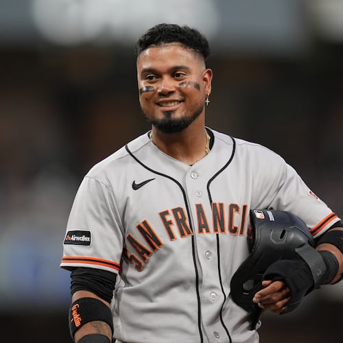 San Francisco Giants' Luis Arraez jokes with players in the San Diego Padres dugout as he stands on first base after getting hit by a pitch during the fourth inning of a baseball game Thursday, July 30, 2026, in San Diego. (AP Photo/Gregory Bull)