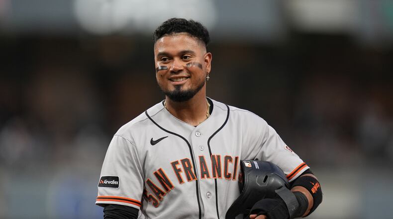 San Francisco Giants' Luis Arraez jokes with players in the San Diego Padres dugout as he stands on first base after getting hit by a pitch during the fourth inning of a baseball game Thursday, July 30, 2026, in San Diego. (AP Photo/Gregory Bull)