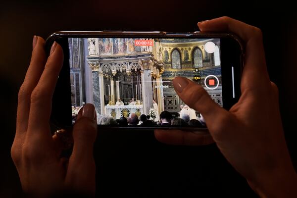 A woman takes photos with her phone to Pope Leo XIV presides over a Mass in the Archbasilica of St. John Lateran and takes possession of the Roman Cathedra, formalising his role as Bishop of Rome in Rome, Sunday, May 25, 2025. (AP Photo/Gregorio Borgia)