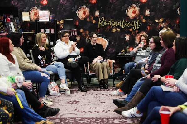 Madison Coleman (center, seated in wing chair) leads a book club discussion about  “Heated Rivalry” at All the Tropes Bookstore in Atlanta. Coleman is the store's social media manager and came up with the idea for this group. (Abbey Cutrer/AJC)