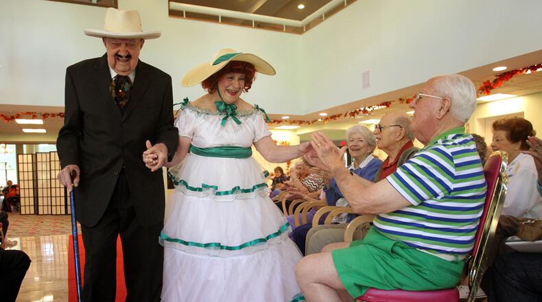Dressed as Rhett and Scarlett Butler, Salty and Lillian Wyatt walk down the red carpet as they greet Lew Fuller (seated) during the Delmar Darlin's and Gent's performance at Delmar Gardens of Gwinnett Friday afternoon in Lawrenceville.