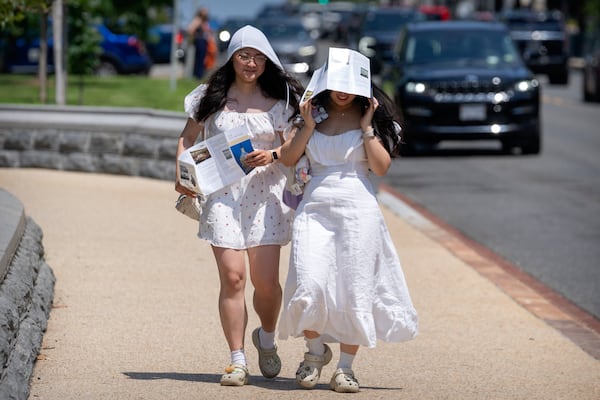 Visitors use brochures to shield themselves from the sun as they walk near the U.S. Capitol on an unseasonably hot day, Tuesday, June 24, 2025, in Washington. (AP Photo/Mark Schiefelbein)