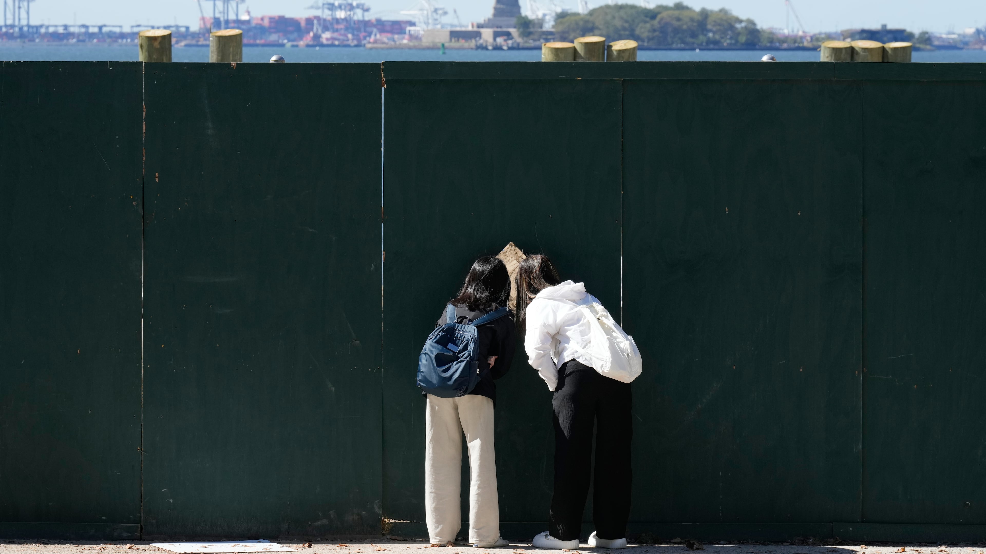People look through fence to get a glance at the Statue of Liberty in New York, Wednesday, Oct. 1, 2025. (AP Photo/Seth Wenig)