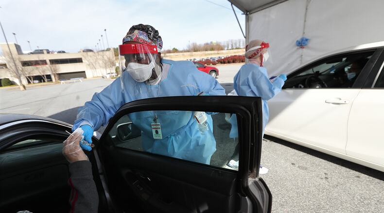 Registered nurses Katrina McCord (left) and Elham Roshanraun (right) work a line of motorists at a free drive-thru COVID-19 DeKalb Board of Health testing site located by the BrandsMart USA while coronavirus testing surges. (Curtis Compton / Curtis.Compton@ajc.com)