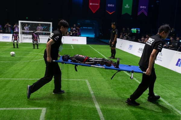 Workers carry out a T1 robot from Booster Robotics during the inaugural RoBoLeague robot soccer competition held in Beijing, Saturday, June 28, 2025. (AP Photo/Ng Han Guan)
