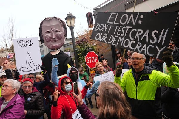 People wave signs and a during a protest against Tesla and Elon Musk outside of a Tesla showroom Saturday, March 29, 2025, in the University District of Seattle. (AP Photo/Lindsey Wasson)