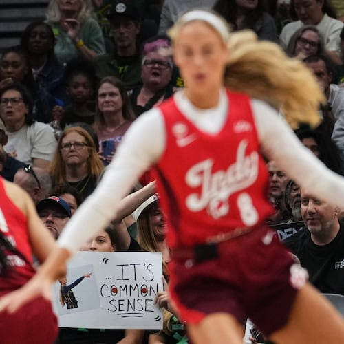 Indiana Fever guard Sophie Cunningham, front, runs by a fan holding a sign referencing her comments on transgender athletes and women's sports during the first half of a WNBA basketball game against the Seattle Storm, Tuesday, July 28, 2026, in Seattle. (AP Photo/Lindsey Wasson)