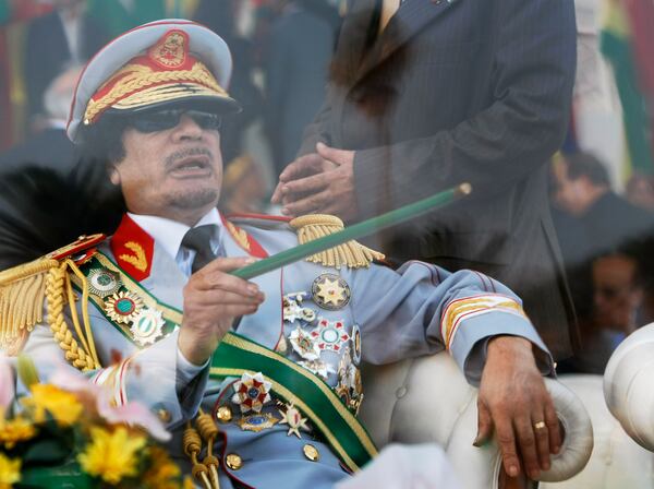 FILE - Libyan leader Moammar Gadhafi gestures with a green cane as he takes his seat behind bulletproof glass for a military parade on Sept. 1, 2009, in Green Square, Tripoli, Libya. (AP Photo/Ben Curtis, File)