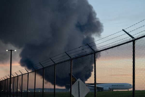 A UPS airplane is seen parked while a plume of smoke from the nearby UPS cargo plane crash is seen at Louisville Muhammad Ali International Airport on Tuesday, Nov. 4, 2025, in Louisville, Ky. (Jon Cherry/AP)