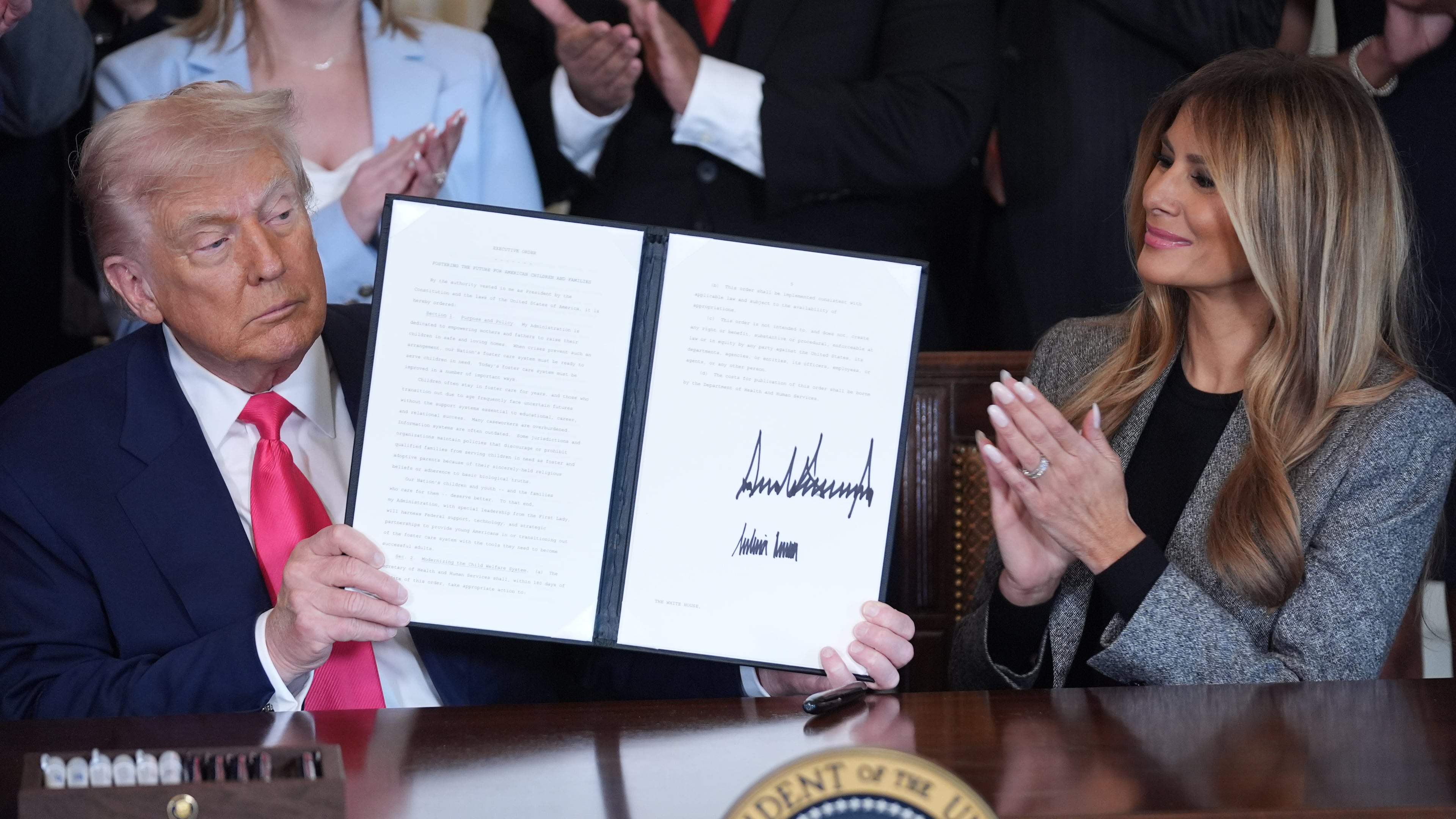 President Donald Trump displays an signed executive order as first lady Melania Trump watches during an event on foster care in the East Room of the at the White House, Thursday, Nov. 13, 2025, in Washington. (AP Photo/Evan Vucci)