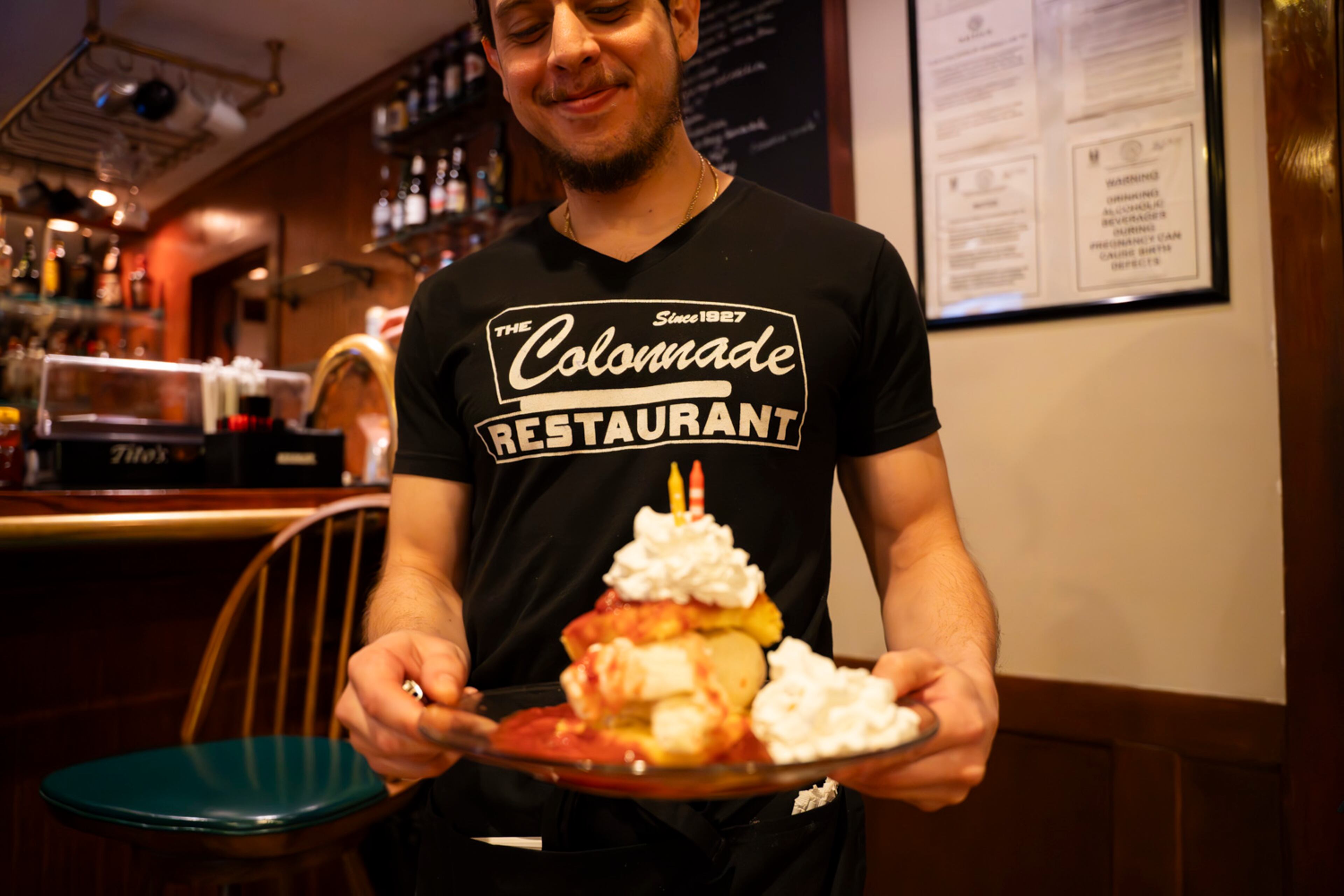 A server delivers a towering plate of strawberry shortcake at the Colonnade, an Atlanta institution with a reputation for catering to “the gays and the grays.” (Olivia Bowdoin for the AJC).