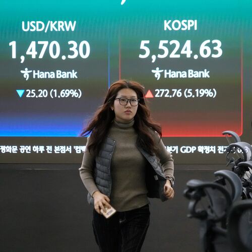 A currency trader passes by a screen showing the Korea Composite Stock Price Index (KOSPI), rear center, and the foreign exchange rate between U.S. dollar and South Korean won, rear left, at the foreign exchange dealing room of the Hana Bank headquarters in Seoul, South Korea, Tuesday, March 10, 2026. (AP Photo/Ahn Young-joon)