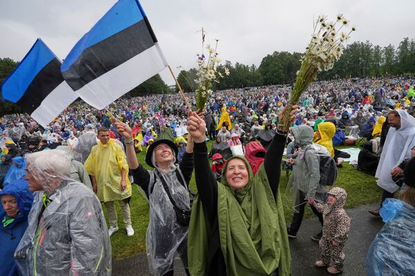 Spectators wave Estonian flags and bouquets of flowers during the song festival, part of the "Iseoma" Song and Dance Celebration, at the Song Festival Grounds in Tallinn, Estonia, Sunday, July 6, 2025. (AP Photo/Sergei Grits)