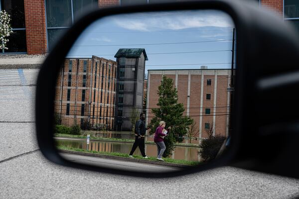In a reflection, community members walk near the flooded Buffalo Trace Distillery on Monday, April 7, 2025, in Frankfort, Ky. (AP Photo/Jon Cherry)