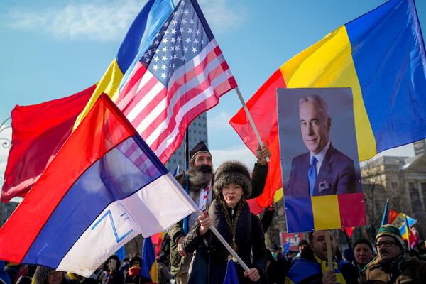 FILE - People wave Russian, U.S. and Romanian flags next to a portrait of Calin Georgescu, the winner of Romania's first round of presidential election which the Constitutional Court later annulled, during a protest in Bucharest, Romania, Feb. 21, 2025. (AP Photo/Vadim Ghirda, File)