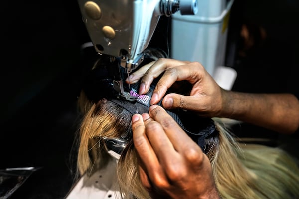 Shamir Wallace, a wig maker, sews his brand's label onto a custom glueless lace wig, Thursday, May 8, 2025, at his salon suite in Atlanta. (AP Photo/Stephanie Scarbrough)