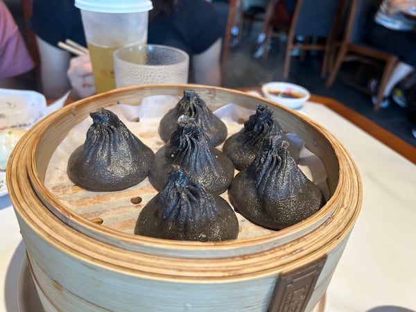 6 xiao long baos dyed black with squid ink, in a bamboo steamer.