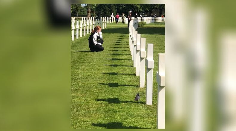 A Hillgrove High School band student kneels at one of the crosses at the Brittany American Cemetery in Normandy, France. Each student found a soldier from Georgia and left a coin in appreciation of their service.