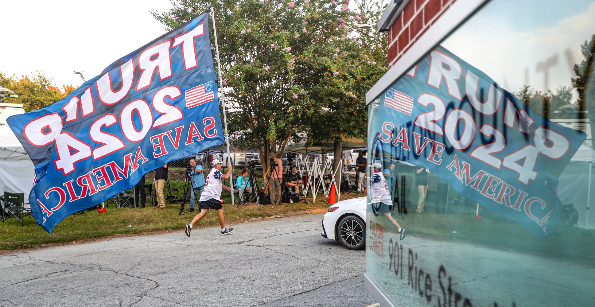 August 24, 2023 Atlanta: Mike Boatman from Evansville, Indiana carries a large Trump flag along Rice Street late Thursday morning, Aug. 24, 2023 where there were more than 100 protestors gathered outside the jail, and they were prepared to wait for hours until the anticipated arrival of former President Donald Trump this afternoon.  (John Spink / John.Spink@ajc.com)


