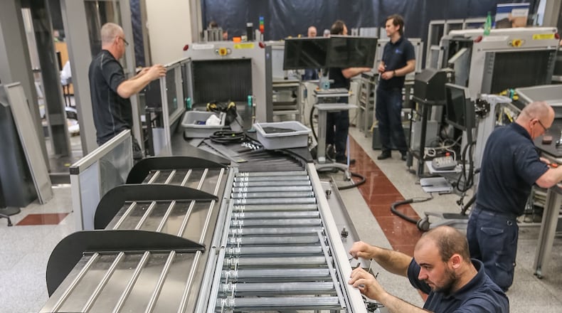 A new lane while it was under construction in early May. The stations on the left allow five different travelers to load bins, each at their own pace. After loading a bin, the traveler pushes the bin onto the automated conveyor system on the right, which will shuttle the bin to the X-ray machine. The passenger can then walk through screening without waiting for slower passengers in front to finish loading bins. John Spink / AJC