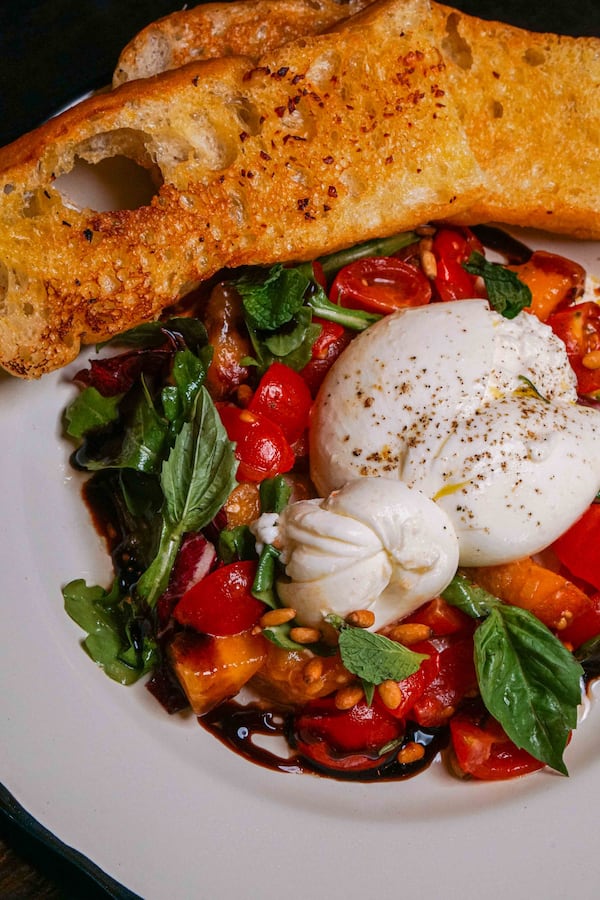 Overhead shot of a burrata salad with tomatoes and arugula, with focaccia on the side.