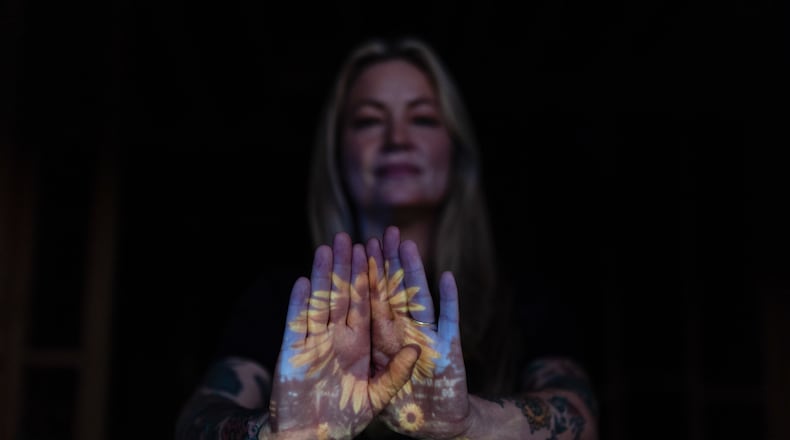 A photo of sunflowers Missi Dowd-Figueroa once grew on her property is projected onto her palms as she poses for a portrait at her rebuilding site in Altadena, Calif., Friday, Dec. 19, 2025, after the Eaton Fire destroyed her home. (AP Photo/Jae C. Hong)