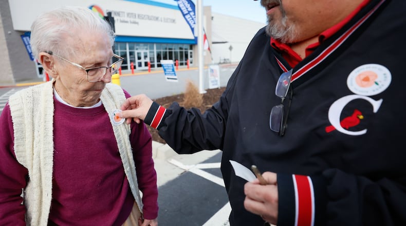 Bill Stephens places a sticker on the vest of his 95-year-old mother, Arline Stephens, after both cast their votes in Gwinnett County during the first day of early voting in the Georgia presidential primary in February. Miguel Martinez/AJC