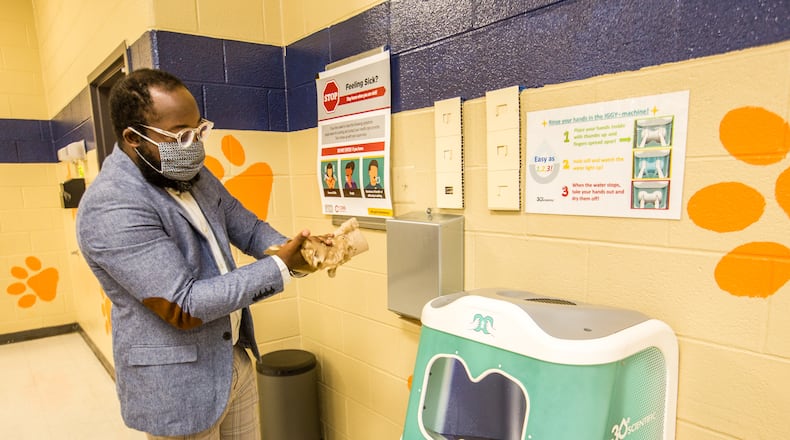 Cobb school board member-elect Tre Hutchins, whose 11-year-old son attends Bryant Elementary School, dries his hands after using "Iggy", 30e Scientific's first aqueous ozone hand washing station is the school's cafeteria in Mableton. The sanitation station uses ozone, a natural disinfectant, to clean elementary school hands in seven seconds before students pick up their school lunches.  The Cobb County School District and the makers of the three sanitation systems installed at the school share information before moving into demonstrates of the technologies Wednesday, Oct 21, 2020.  (Jenni Girtman for The Atlanta Journal-Constitution)