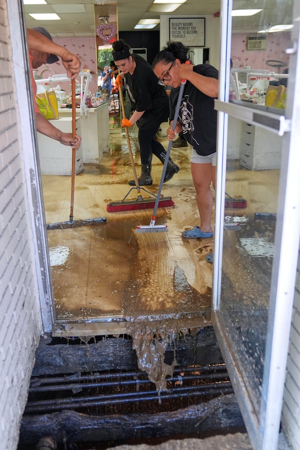 Heylin Gonzales, right, Heidy Ayala, center, and others brush water into a hole that a flood opened up on the stoop of the Glow'n Beauty Bar in North Plainfield, N.J., Tuesday, July 15, 2025. (AP Photo/Seth Wenig)