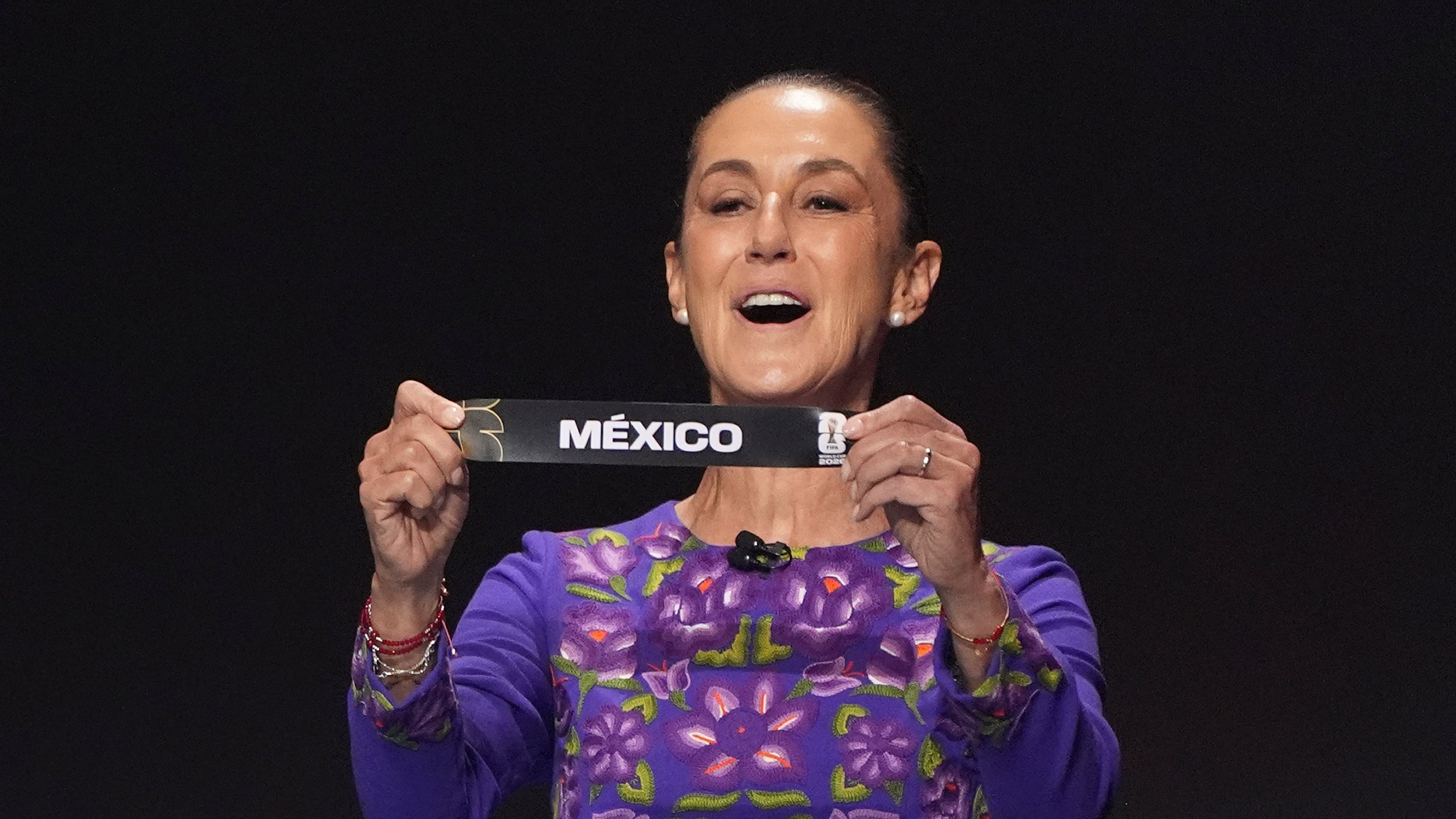 Mexican President Claudia Sheinbaum holds up the team name of Mexico during the draw for the 2026 soccer World Cup at the Kennedy Center in Washington, Friday, Dec. 5, 2025.(AP Photo/Evan Vucci)