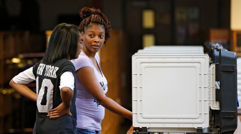 Zhane Johnson, 14, watches as her mother, Cassandra, casts her ballot at Mary Mcleod Bethune Middle School in Decatur in July. BOB ANDRES / BANDRES@AJC.COM