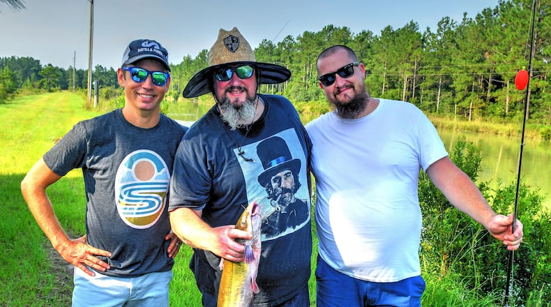 Zack Gowan (from left, owner of Georgia Sea Grill, Satilla Ponds and Potlikker Farms), Tim Lensch (executive chef at Georgia Sea Grill) and Eric Miller (Satilla Ponds farm operator) pose with a just-caught catfish Sunday morning. Chris Hunt for The Atlanta Journal-Constitution