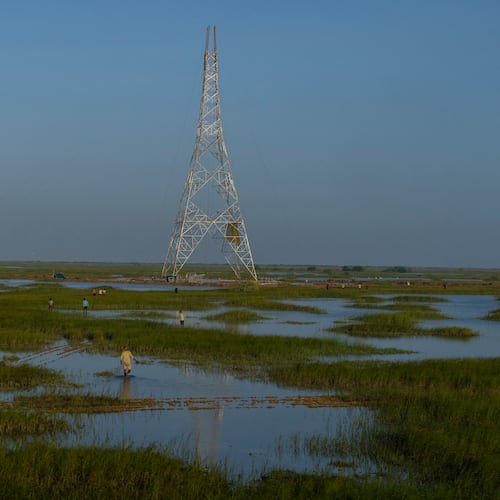 FILE - Workers walk through a swamp to install electric transmission towers for the Adani Renewable Energy Park near Khavda, Bhuj district, near the India-Pakistan border in the western state of Gujarat, India, Sept. 21, 2023. (AP Photo/Rafiq Maqbool, File)