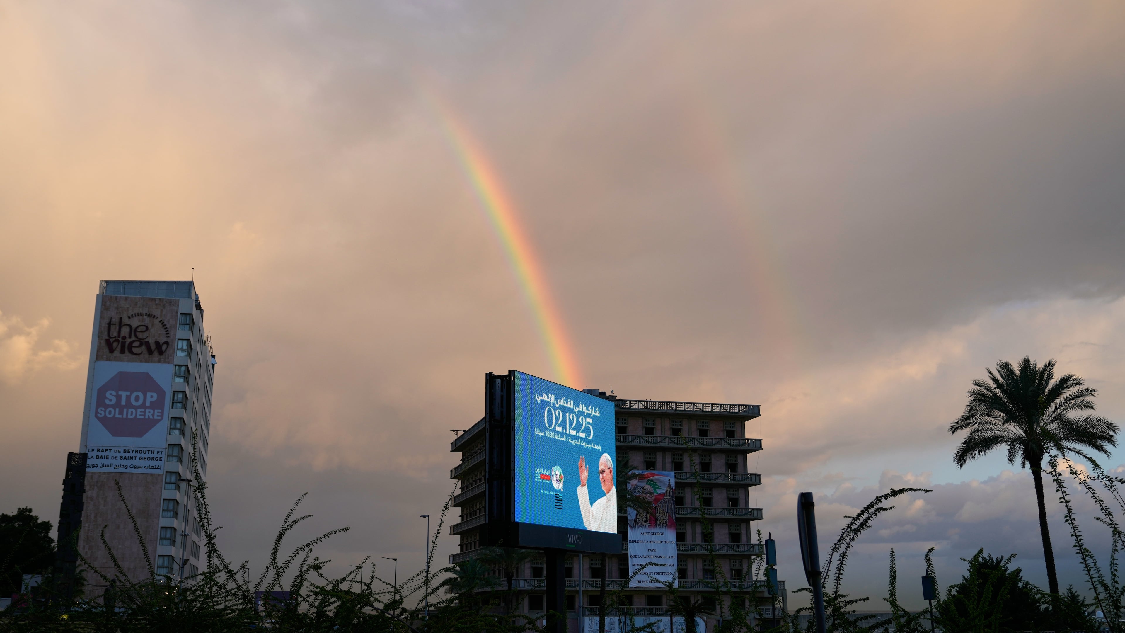 A rainbow rises behind a billboard featuring Pope Leo XIV in Beirut, Lebanon, Monday, Dec. 1, 2025. (AP Photo/Hassan Ammar)