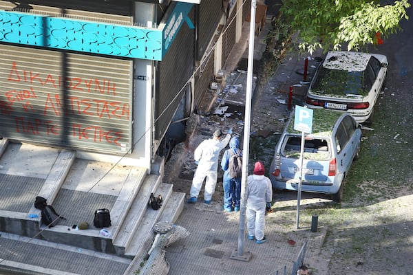 Greek police forensic experts search the area where a 38-year-old woman was killed early Saturday when a bomb she was carrying exploded in her hands outside a bank branch, local police said, in Thessaloniki, northern Greece, May 3, 2025. On the fence of the bank branch reads : "Justice is to resist. Take stones". (AP Photo/Giannis Papanikos)