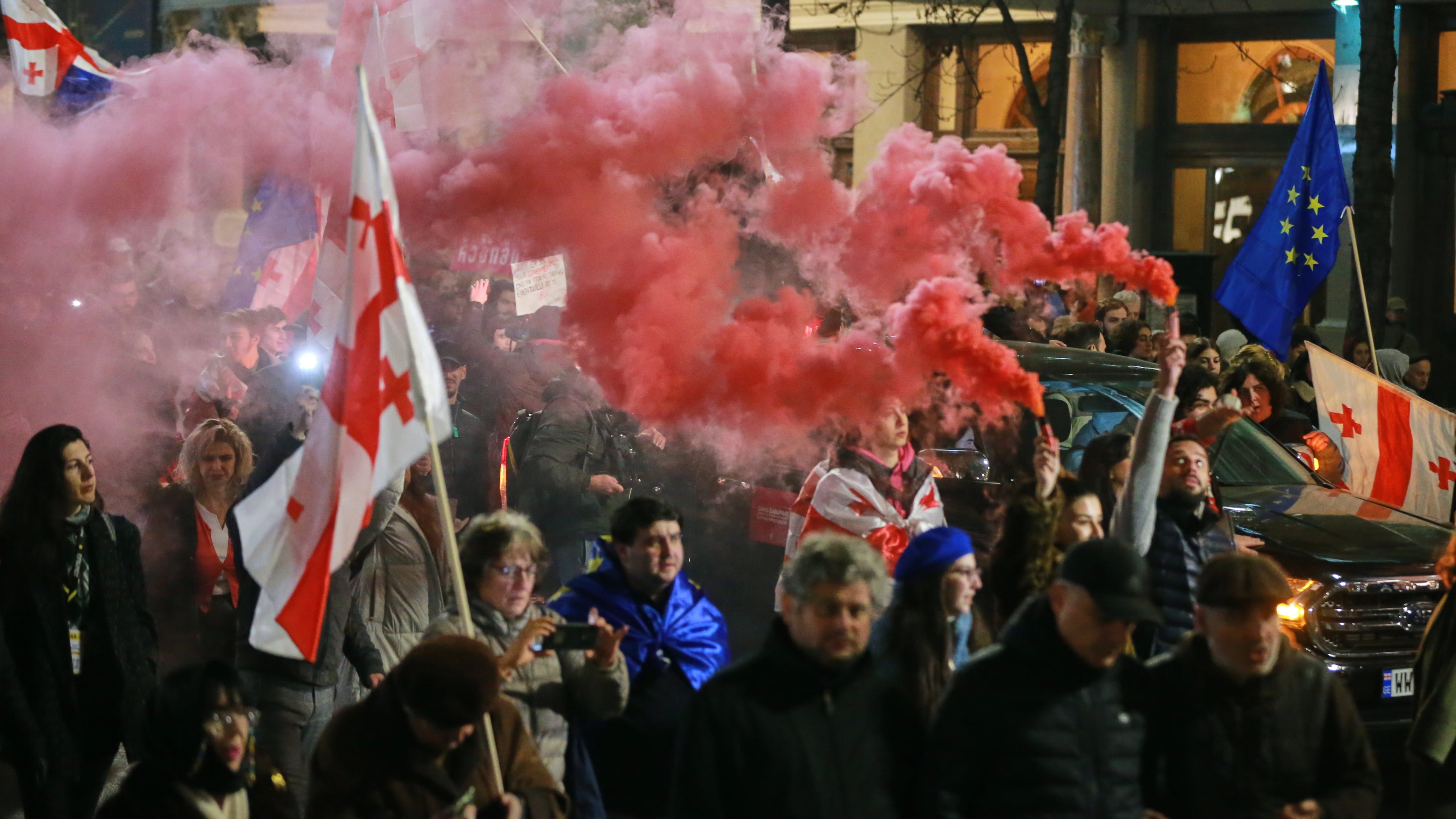 Demonstrators with Georgian and EU flags light flares as they gather in the Georgian capital of Tbilisi, on Friday, Nov. 28, 2025, to mark 365 days of non-stop protests against the government's decision to halt talks on joining the European Union. (AP Photo/Zurab Tsertsvadze)