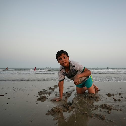 A boy plays in wet sand as others swim and commercial vessels lie anchored in the Strait of Hormuz off Bandar Abbas, Iran, Friday, Sept. 4, 2026. (AP Photo/Vahid Salemi)