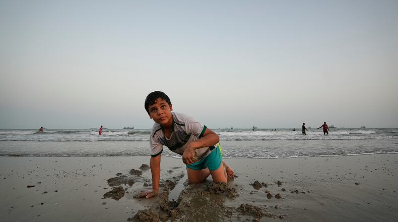 A boy plays in wet sand as others swim and commercial vessels lie anchored in the Strait of Hormuz off Bandar Abbas, Iran, Friday, Sept. 4, 2026. (AP Photo/Vahid Salemi)